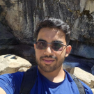 Young man wearing sunglasses and blue shirt, smiling with rocky cliff background