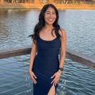 Young woman with dark hair in navy dress, standing on a lakeside wooden dock at sunset