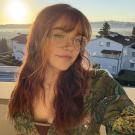 Young woman with glasses smiling at sunset on a balcony, houses and water in background