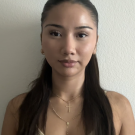 Young woman portrait, long dark hair, neutral face, yellow top, gold layered necklaces